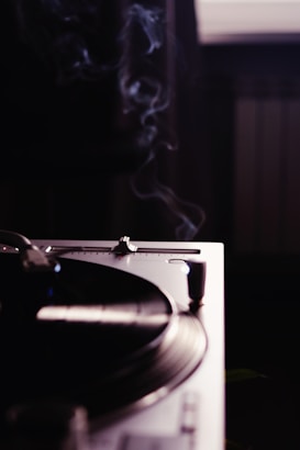 A close-up view of a turntable with a vinyl record spinning, emanating an aura of nostalgia and classic music ambiance. Wisps of smoke rise gently in the dimly lit room, adding a serene and vintage atmosphere.