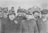 A group of young male miners wearing work jackets and headlamps smile towards the camera. They appear to be taking a break from their work, standing closely together in a friendly and relaxed manner.