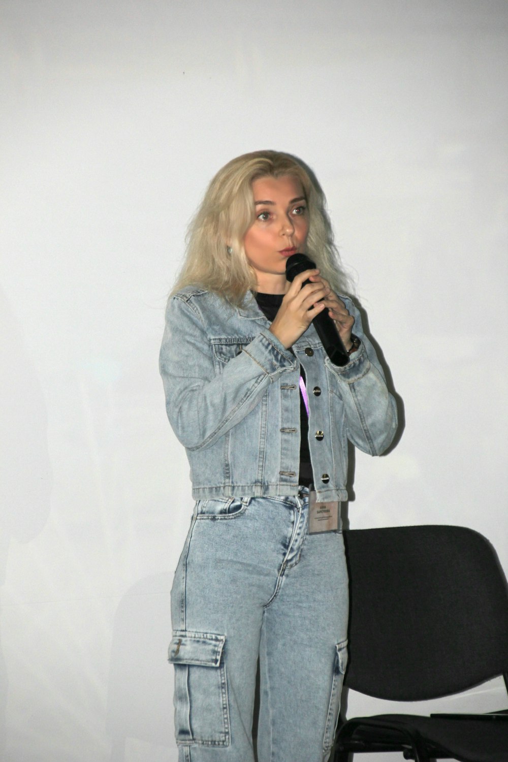 a woman standing in front of a white wall holding a microphone