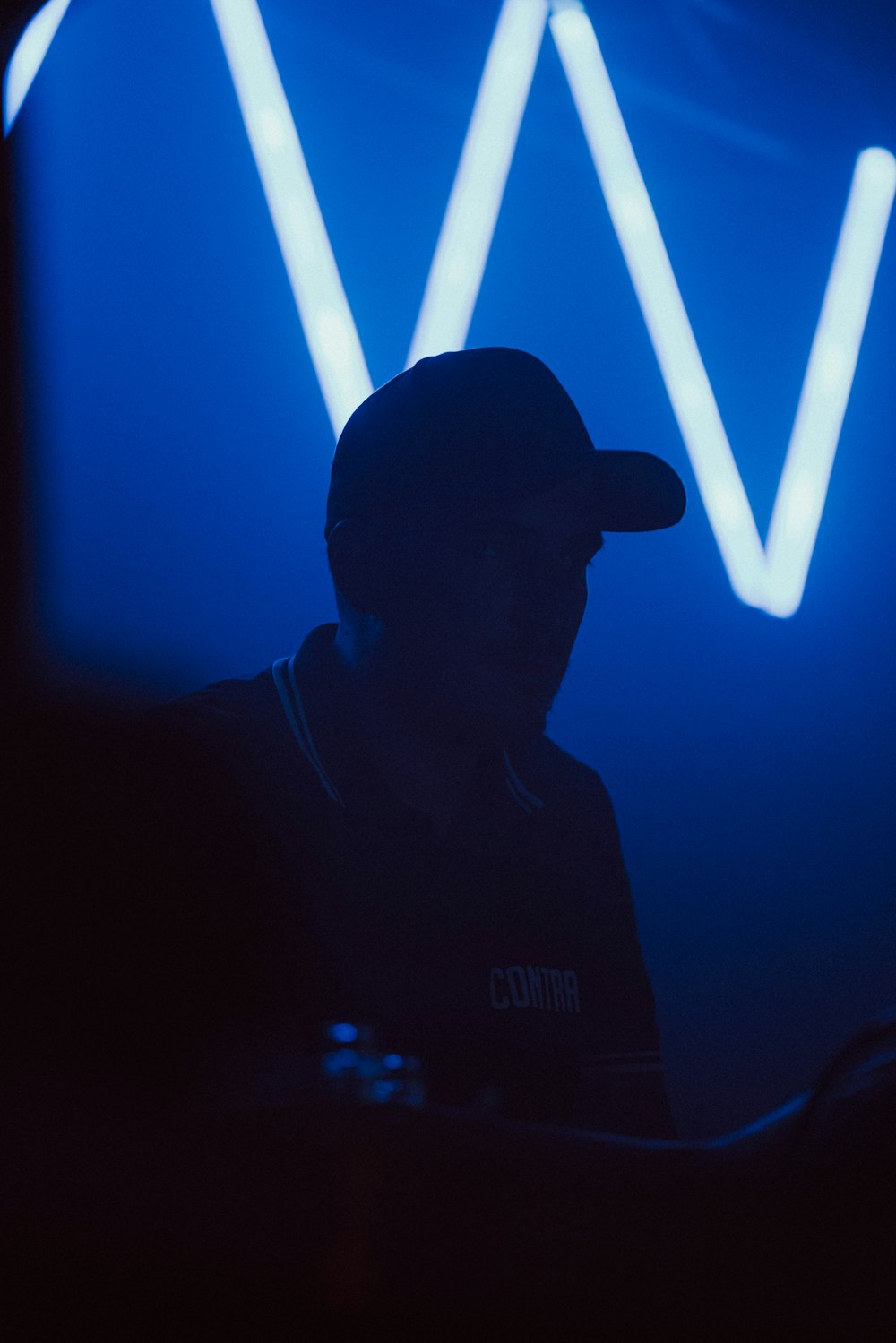 a man in a baseball cap sitting in front of a neon sign