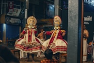 Traditional Kathakali dancers in elaborate costumes and makeup performing a dramatic scene.