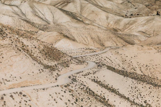 Wide shot of rugged terrain with sparse desert vegetation and a dirt road.