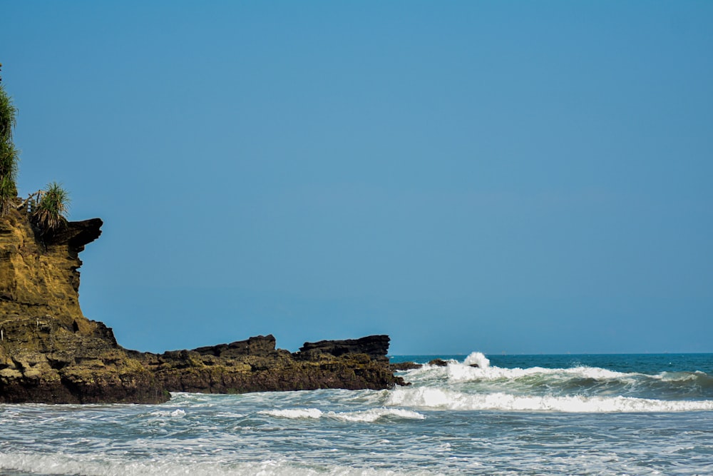 a rock outcropping on a beach with waves crashing in front of it