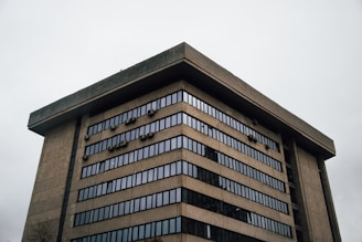 A large, multi-story concrete building with rows of windows. The architecture appears modern with an emphasis on functional design, featuring numerous small, box-like elements attached to the exterior.