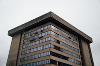 A large, multi-story concrete building with rows of windows. The architecture appears modern with an emphasis on functional design, featuring numerous small, box-like elements attached to the exterior.