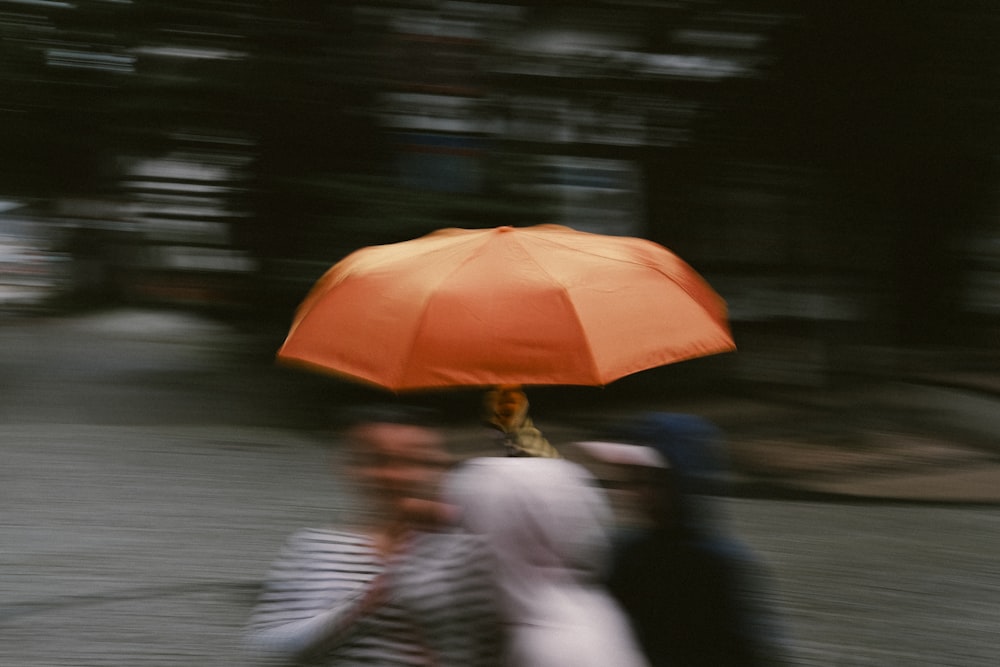 a group of people walking down a street under an orange umbrella