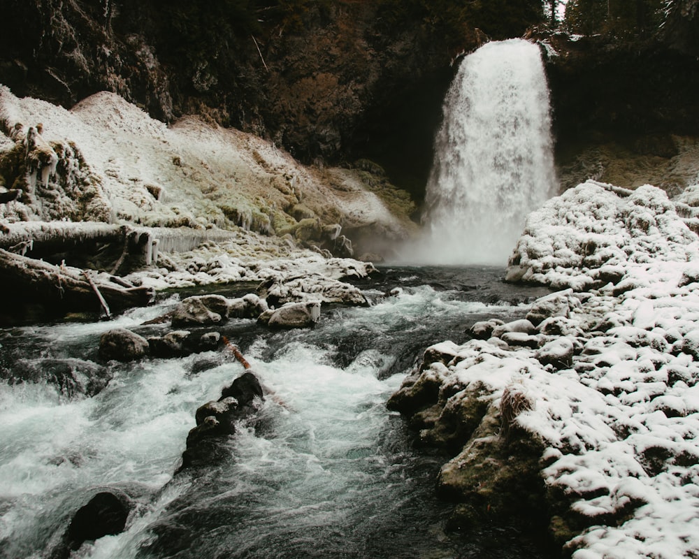 a small waterfall is surrounded by snow and rocks