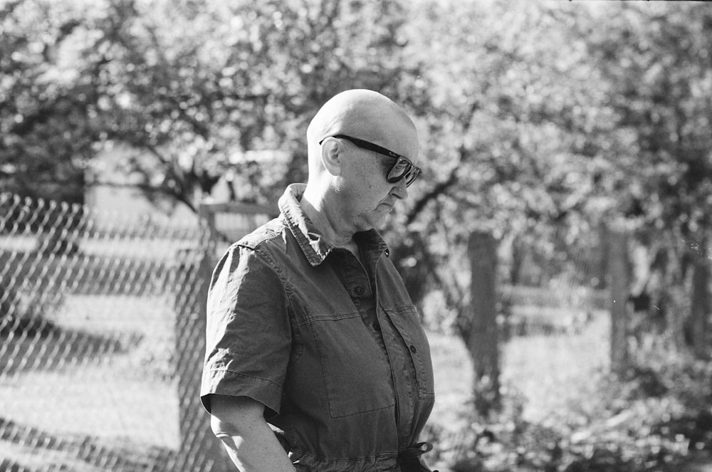 a man with a bald head and glasses standing in front of a fence
