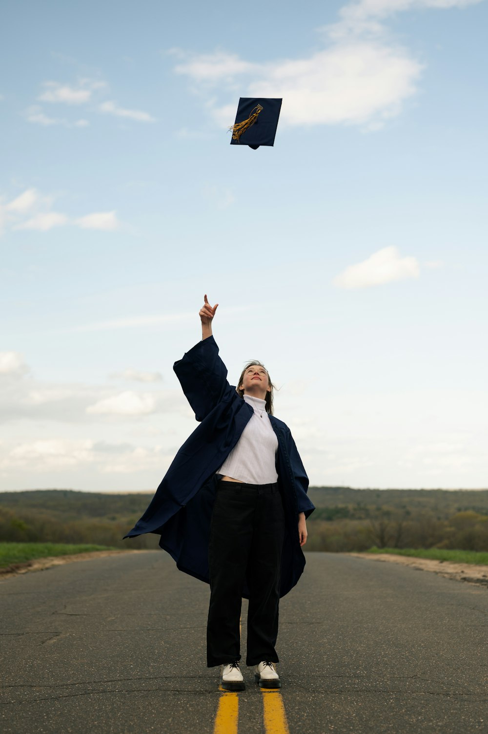 a woman standing on the side of a road flying a kite