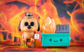 A cartoon-style dog character with black eyes and a brown hat sits next to a dumpster that has a smiling face. Flames are rising from the dumpster, and the dog holds a sign that reads 'This is fine.' The background is filled with vibrant orange and yellow flames, creating a sense of chaos.