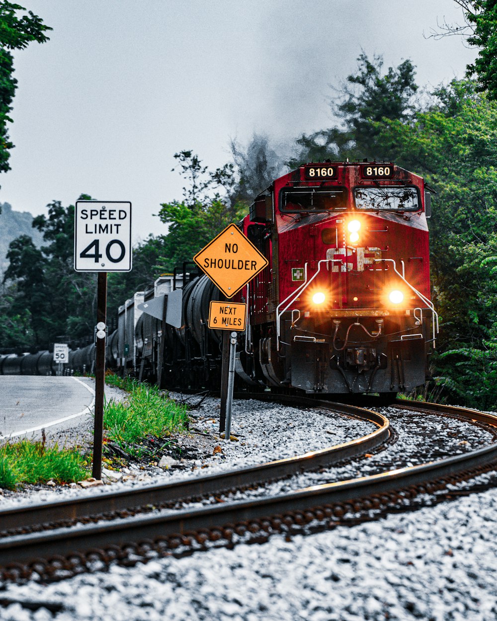 a red train traveling down train tracks next to a forest