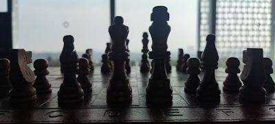 A silhouette of wooden chess pieces arranged on a chessboard, set against a bright window, creating a stark contrast between light and dark.