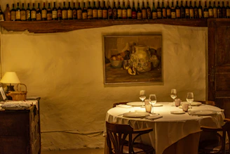 A cozy dining setup featuring a warm wood 4-seat table with linen pillows on chairs and a glass candle stand softly glowing.