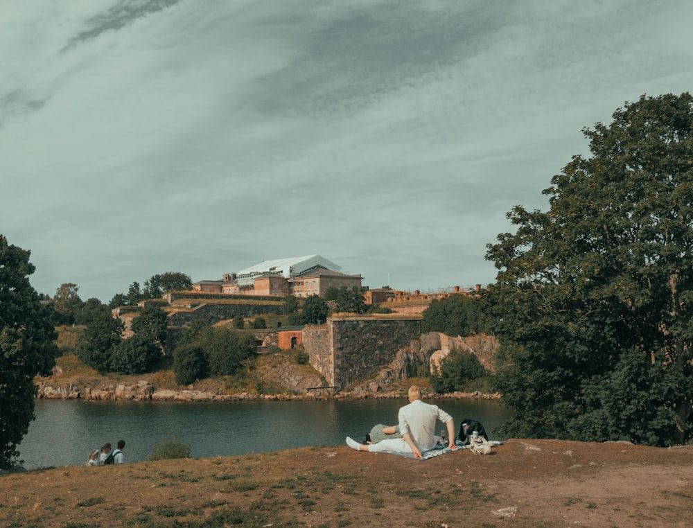 a man sitting on a hill next to a body of water