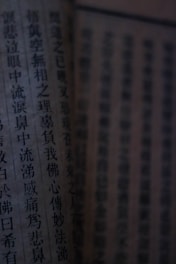 Close-up view of a page from a book, featuring vertical lines of Chinese characters. The lighting is dim, casting shadows and giving the page an aged appearance.