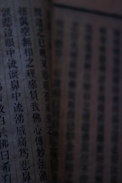 Close-up view of a page from a book, featuring vertical lines of Chinese characters. The lighting is dim, casting shadows and giving the page an aged appearance.