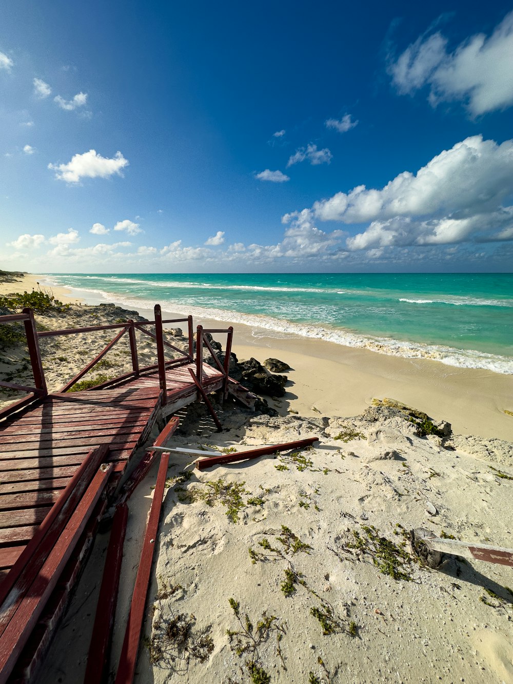 a wooden walkway leading to the beach on a sunny day