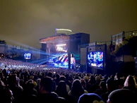 A drone shot capturing a large outdoor concert crowd with colorful stage lighting and LED screens.
