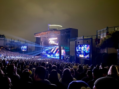 A massive outdoor concert stage with bright lights and a packed crowd at dusk.