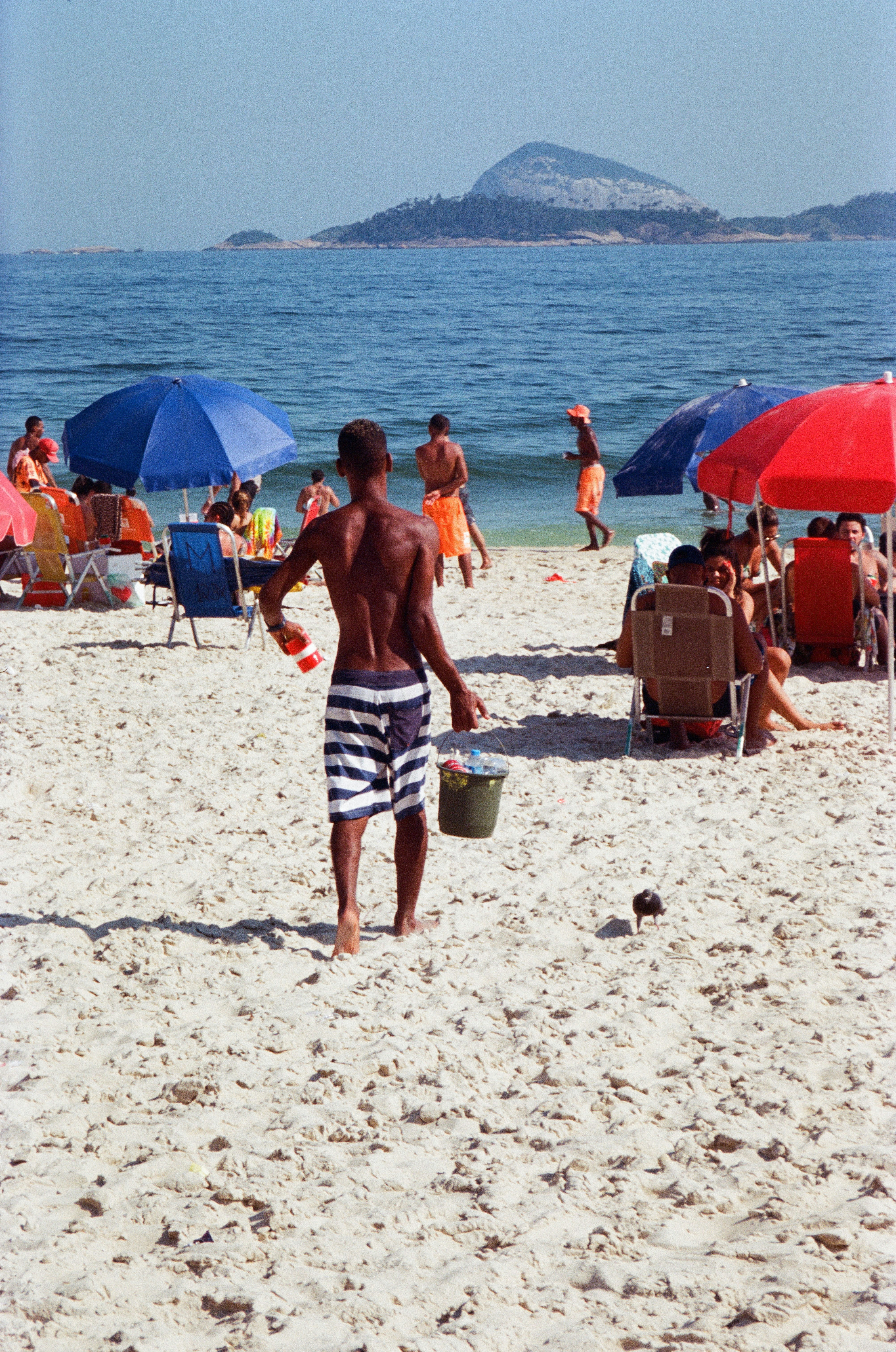 a man walking on the beach with a bucket of sand