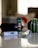 A tube of L'Occitane product is centered on a sleek reflective surface. Surrounding it are other skincare tubes and a decorative vase with green and white stripes. The background is softly blurred, creating a serene and elegant atmosphere.