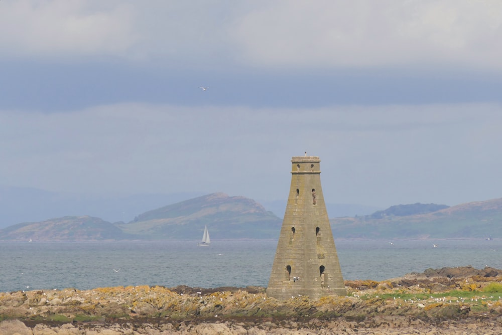 a stone tower with a sailboat in the background