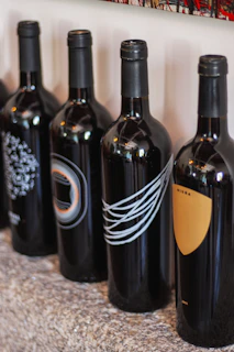 Artistic arrangement of several custom wine bottles showcasing different vinyl designs on a light parchment background.