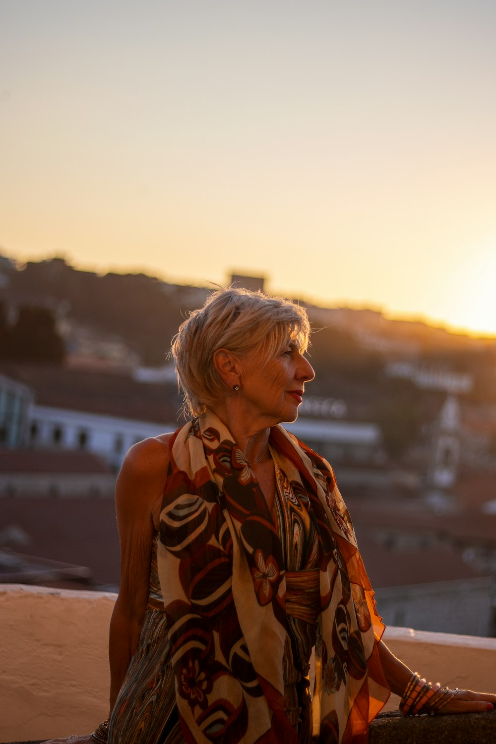 a woman is sitting on a ledge at sunset