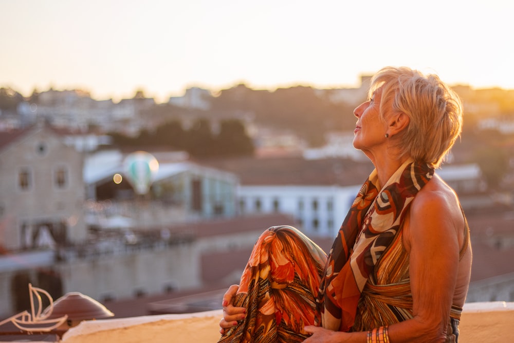 a woman sitting on a ledge with a city in the background