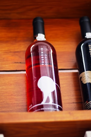 A bottle of red or ros&eacute; wine displayed on a wooden shelf. The label reads 'Tour&oacute;nio Douro' and features a minimalist design with a silhouette of a person bending over. The bottle is next to another wine bottle that is partially visible.