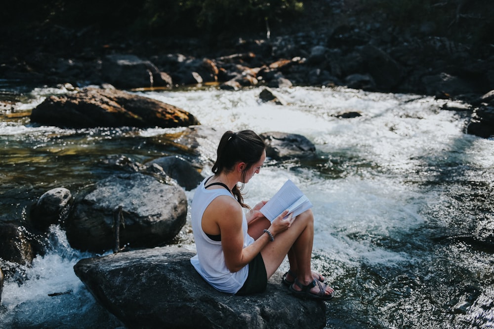 a woman sitting on a rock reading a book