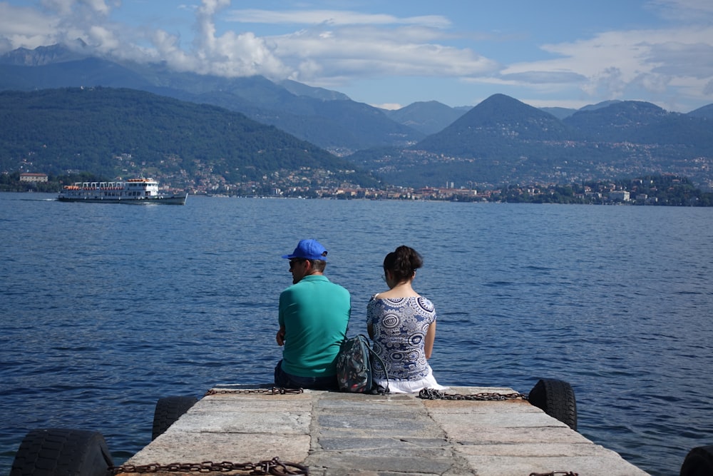 a man and a woman sitting on a pier looking out at the water