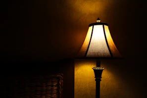 A ceramic table lamp with a textured linen shade casting a soft light on a bedside table.
