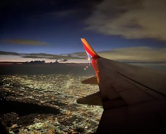 A sleek, dark blue airplane wing cutting through a twilight sky, with city lights twinkling below.