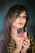 A smiling woman with flawless makeup holding a trendy lipstick in a cozy, well-lit room.