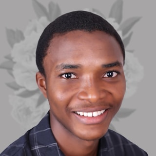 A person with a bright smile and short black hair, wearing a black and white checkered shirt. The background is gray with floral designs.