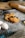 A baking scene features flaky pastries with chocolate, resting on a cooling rack dusted with flour. Nearby, fresh eggs, a block of butter, a whisk, and a wooden rolling pin are visible, suggesting a preparation setting. The overall atmosphere conveys a sense of home baking, warmth, and deliciousness.