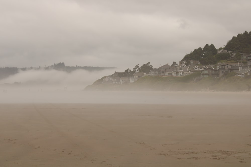 a foggy beach with houses on a hill in the distance