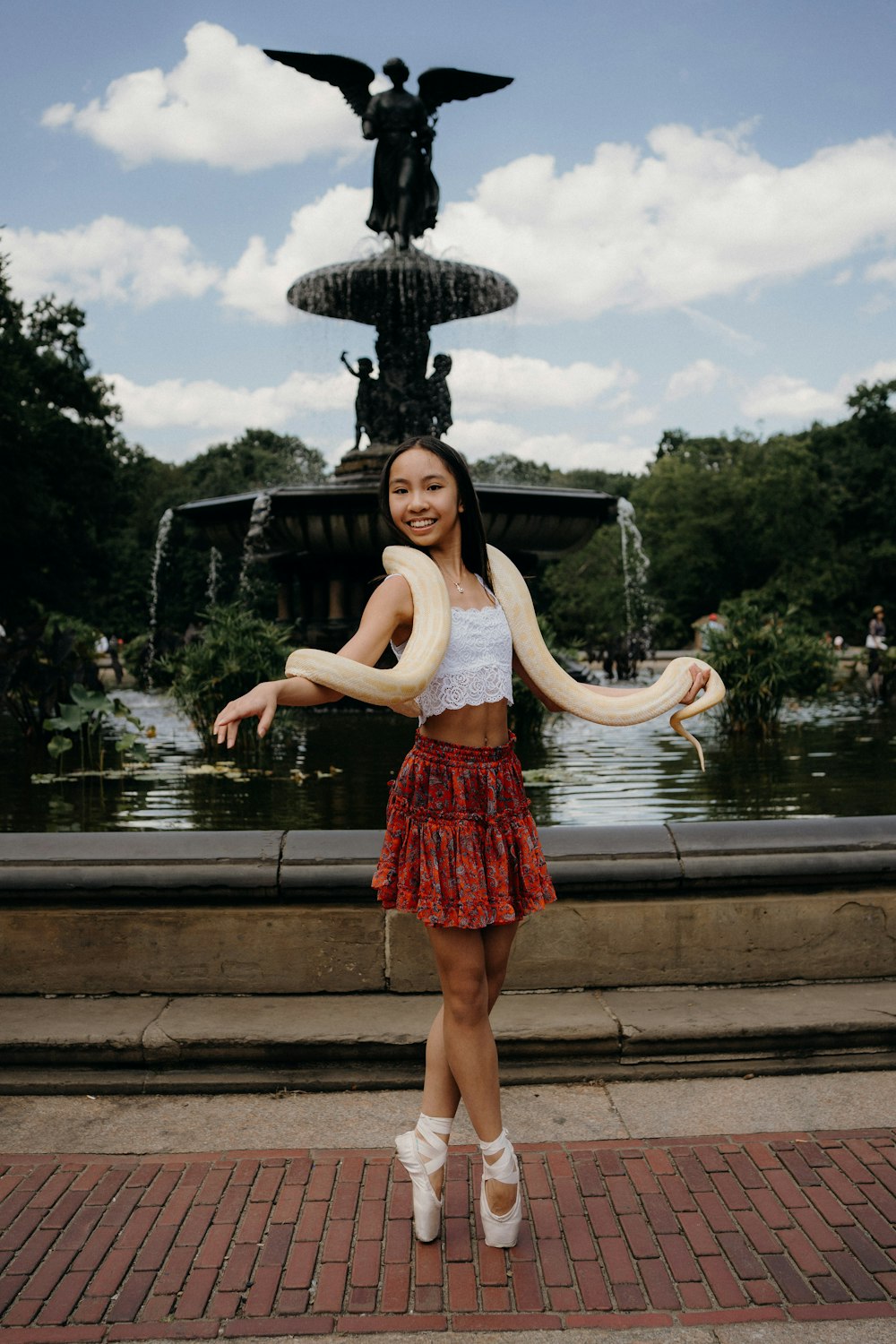 a woman holding a snake in front of a fountain