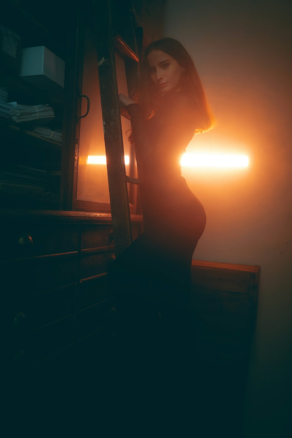 a woman standing in a dark room next to a ladder
