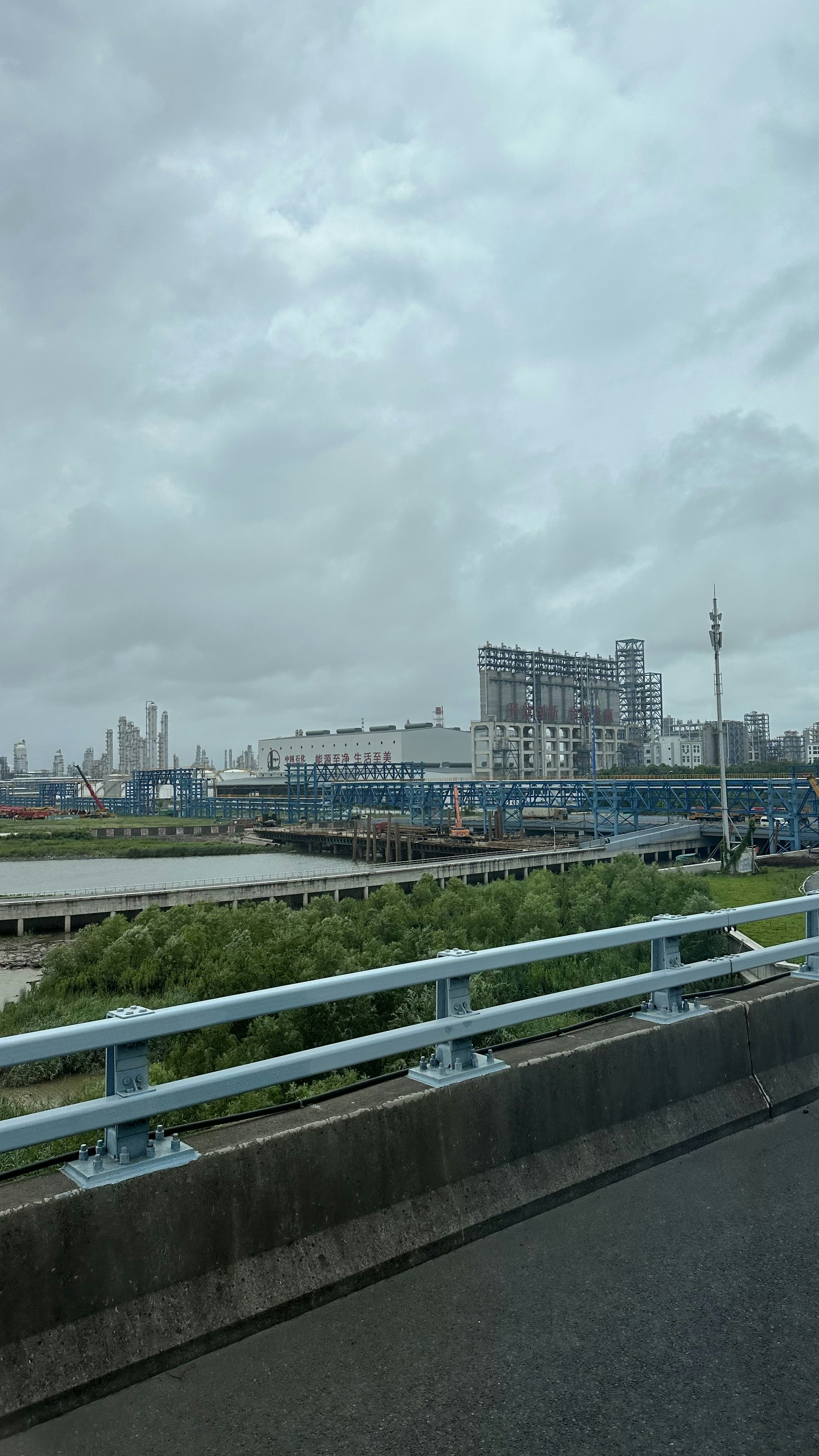 Large industrial pipeline construction through flat terrain, overcast sky, dark steel pipe sections and heavy machinery