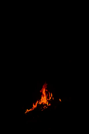 A minimalist black brasero with flickering flames, set against a dark background.