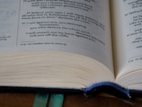 An open book featuring text predominantly in English. The focus is on the text, with visible page numbers and footnotes. A green ribbon bookmark is partially visible at the bottom, and the pages appear slightly curved.