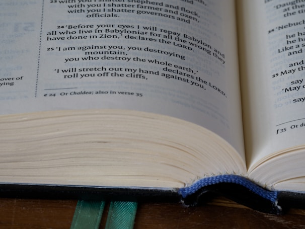 An open book featuring text predominantly in English. The focus is on the text, with visible page numbers and footnotes. A green ribbon bookmark is partially visible at the bottom, and the pages appear slightly curved.