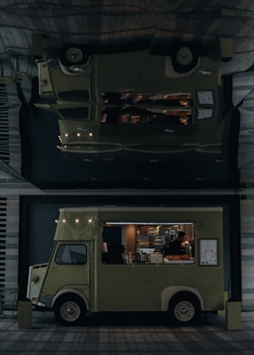 A vintage-style food truck with a pale green color is parked in an urban setting, offering a variety of pastries and beverages. The truck's interior is illuminated, highlighting pastries displayed inside. A person inside the truck is attending to the offerings or setting up. The truck bears the name 'LADUREE' on its side. Its exterior design features classic elements, and a menu board is visible.