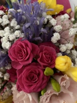A vibrant bouquet of assorted flowers featuring pink roses, purple blooms, yellow buds, and delicate white baby's breath. The arrangement creates a lush, textured appearance with an abundance of petals and varied floral shapes.