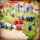 A strategic board game setup features a map of territories with plastic toy soldiers in blue and black positioned across various regions. Red and blue six-sided dice with white dots are scattered among the figures, indicating game moves or outcomes. The terrain colors indicate different zones, enhancing the gaming experience with visual aids.