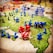 A strategic board game setup features a map of territories with plastic toy soldiers in blue and black positioned across various regions. Red and blue six-sided dice with white dots are scattered among the figures, indicating game moves or outcomes. The terrain colors indicate different zones, enhancing the gaming experience with visual aids.
