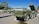 Several military vehicles and missile launch systems are displayed outdoors in a museum-like setting. The vehicles are painted in army green and are positioned on a concrete surface with informational plaques in front of them. In the background, there are trees and utility poles under a clear blue sky.