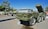 Several military vehicles and missile launch systems are displayed outdoors in a museum-like setting. The vehicles are painted in army green and are positioned on a concrete surface with informational plaques in front of them. In the background, there are trees and utility poles under a clear blue sky.